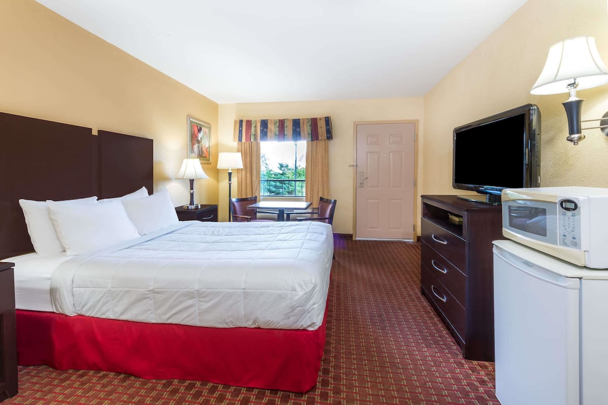 Una habitación de hotel con una cama grande, un escritorio con silla, televisión, microondas y una puerta.