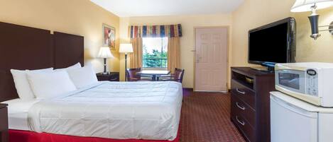 A hotel room with a large bed, a desk with a chair, a television, a microwave, and a door.