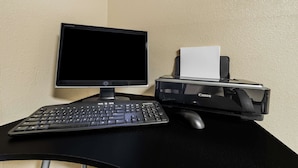 A desktop computer setup with a monitor, keyboard, and Canon printer on a black desk against a beige wall.