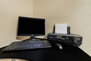 Un equipo de escritorio con monitor, teclado e impresora Canon sobre un escritorio negro frente a una pared color beige.