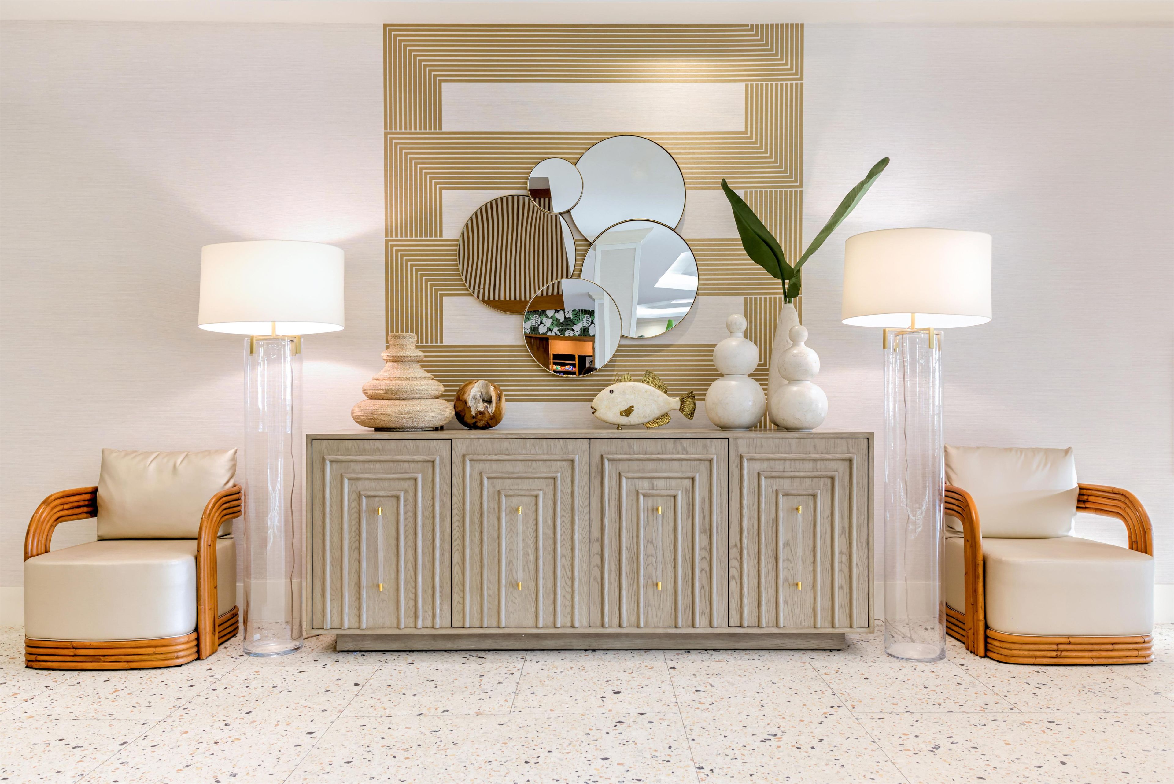 A modern living room with a grey console table, two armchairs, a large mirror, and two floor lamps.