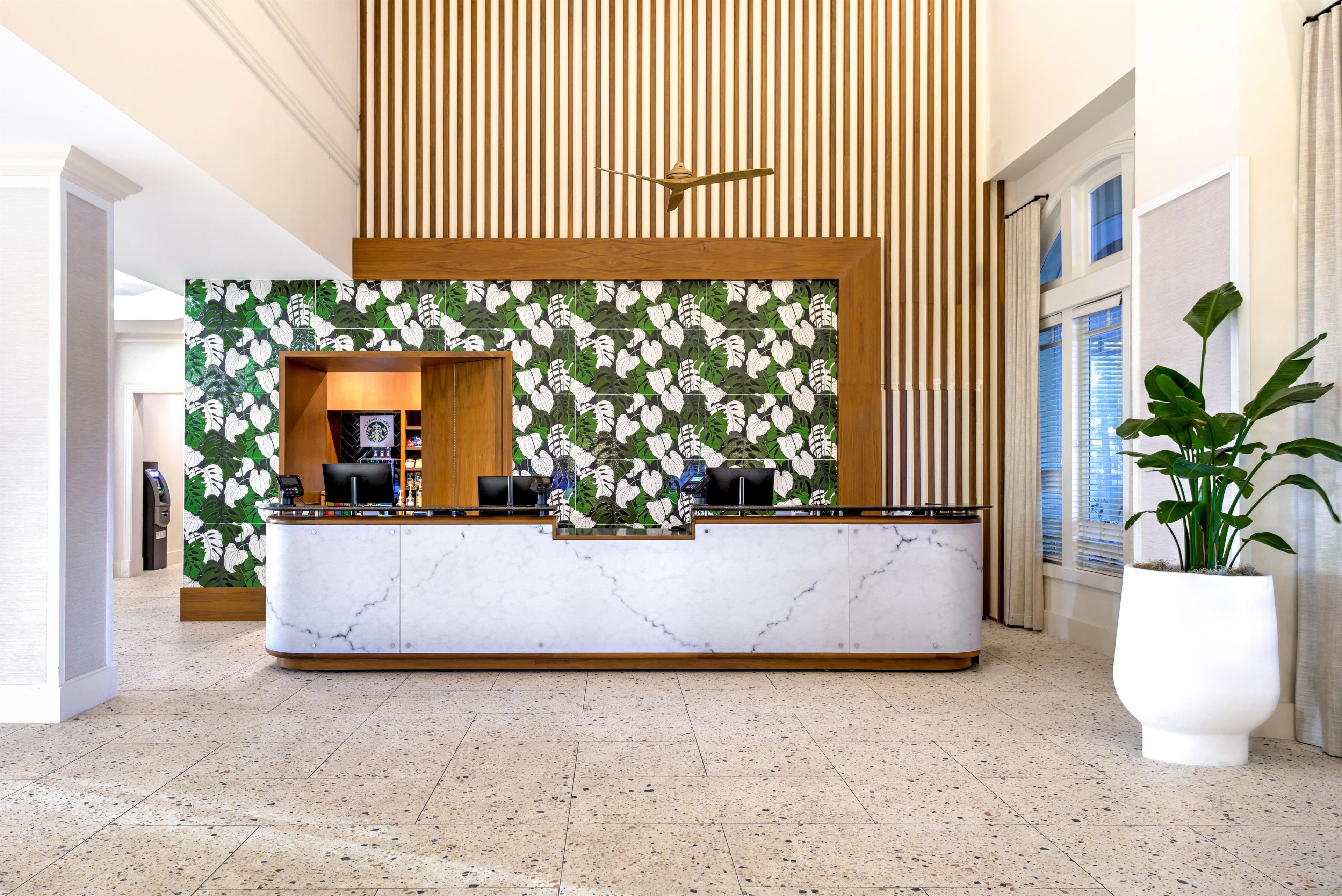 Una reception con pannello in legno sullo sfondo e una parete rivestita di piastrelle con motivo a foglia verde.
