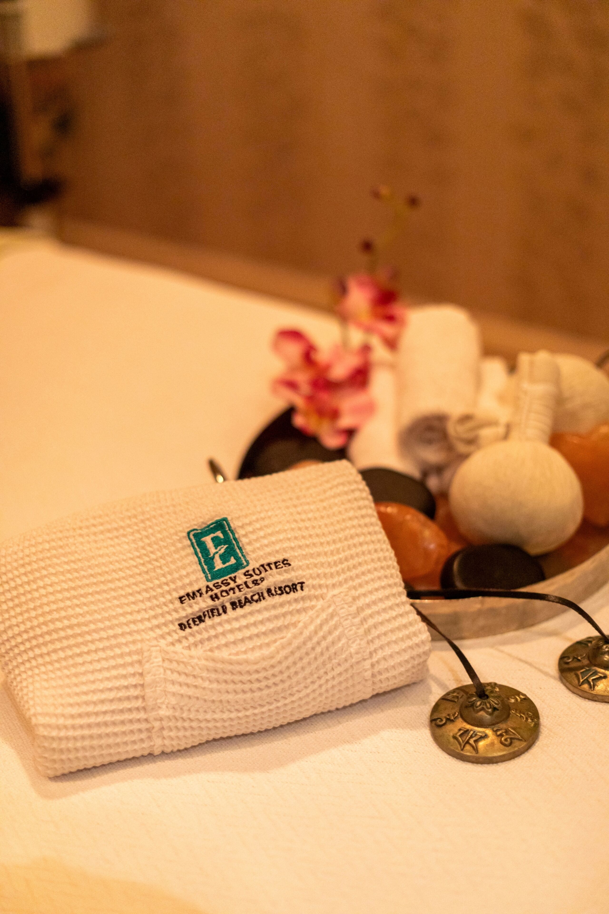 Un ambiente de spa con una toalla, utensilios de masaje y un arreglo floral.