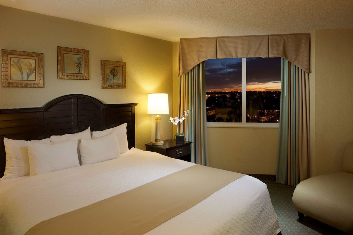 A hotel room with a large bed, a nightstand with a lamp, a window with curtains, and three framed pictures on the wall.
