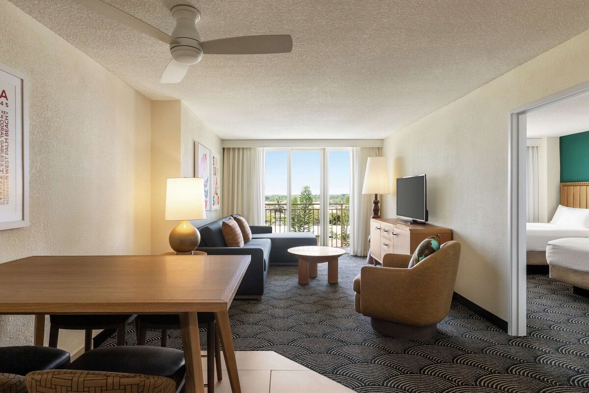 Une chambre d’hôtel avec un coin repas, un canapé, une télévision et un balcon avec vue.