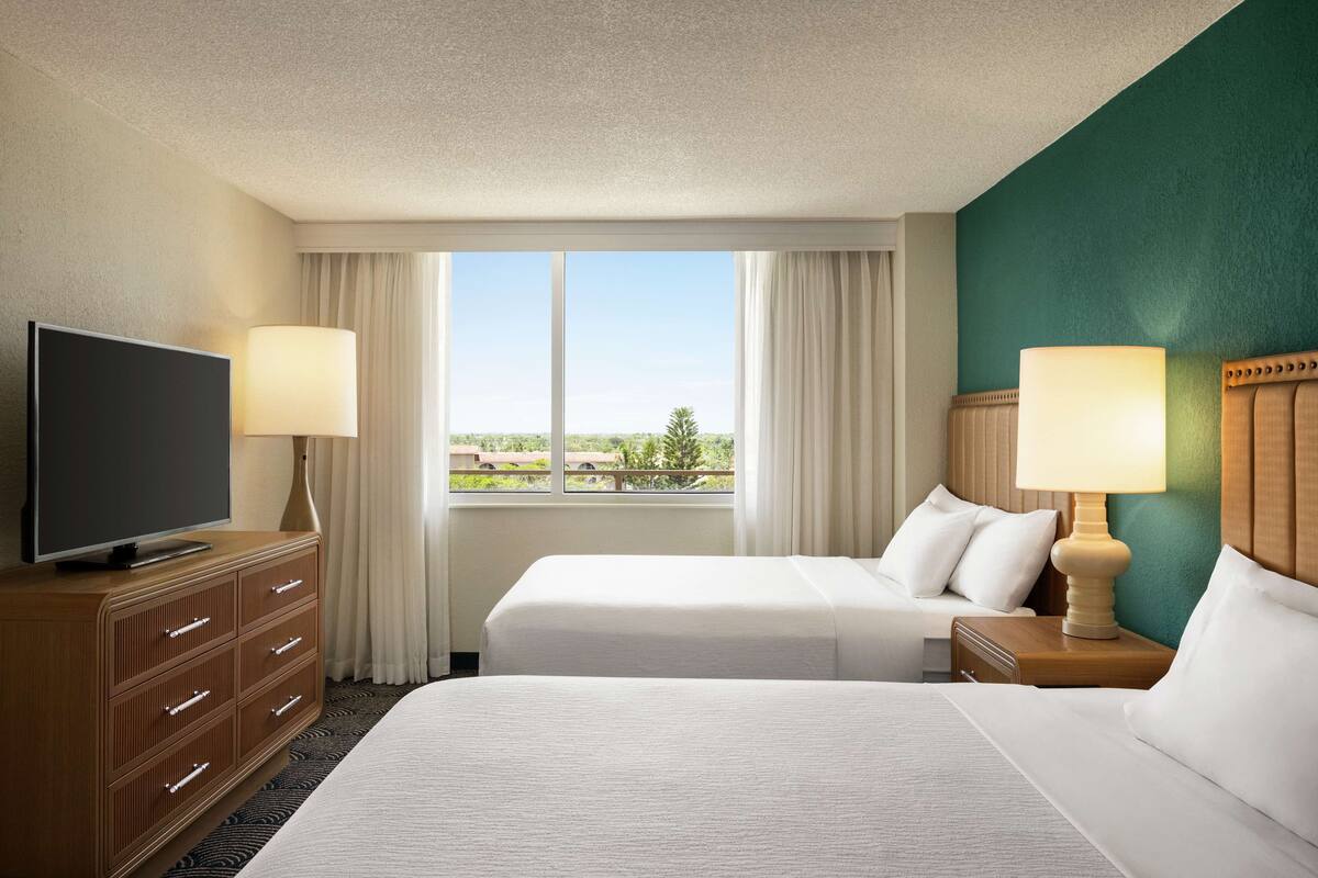 Ein Hotelzimmer mit zwei Betten, einem Fernseher und Blick ins Freie.