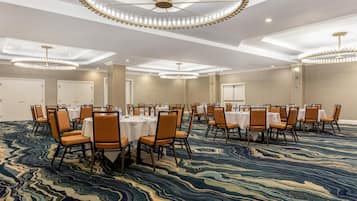 Un salón de conferencias con mesas y sillas redondas, alfombra estampada y un candelabro circular en el techo.