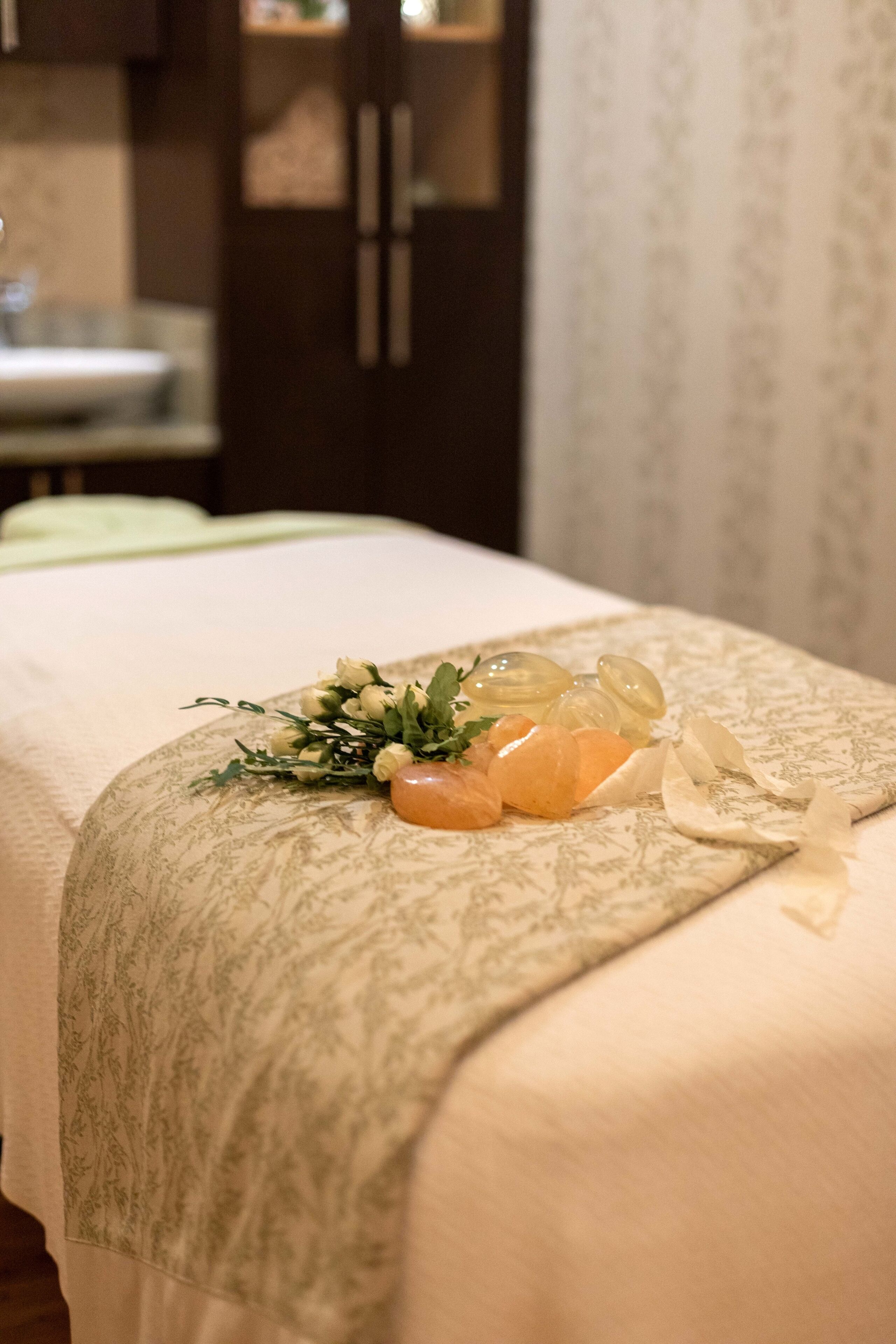 Una cama bien hecha con una colcha de motivos florales, un pequeño ramo de flores y algunas frutas cítricas sobre la cama.