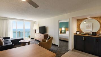 Habitación de hotel con balcón, televisión, cama, escritorio y zona de comedor.