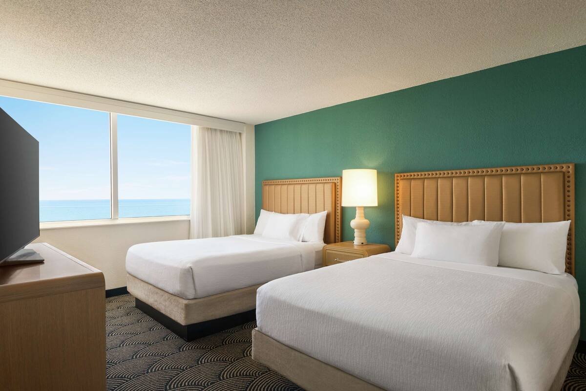 Ein Hotelzimmer mit zwei Betten, einem Fernseher und einem Fenster mit Meerblick.