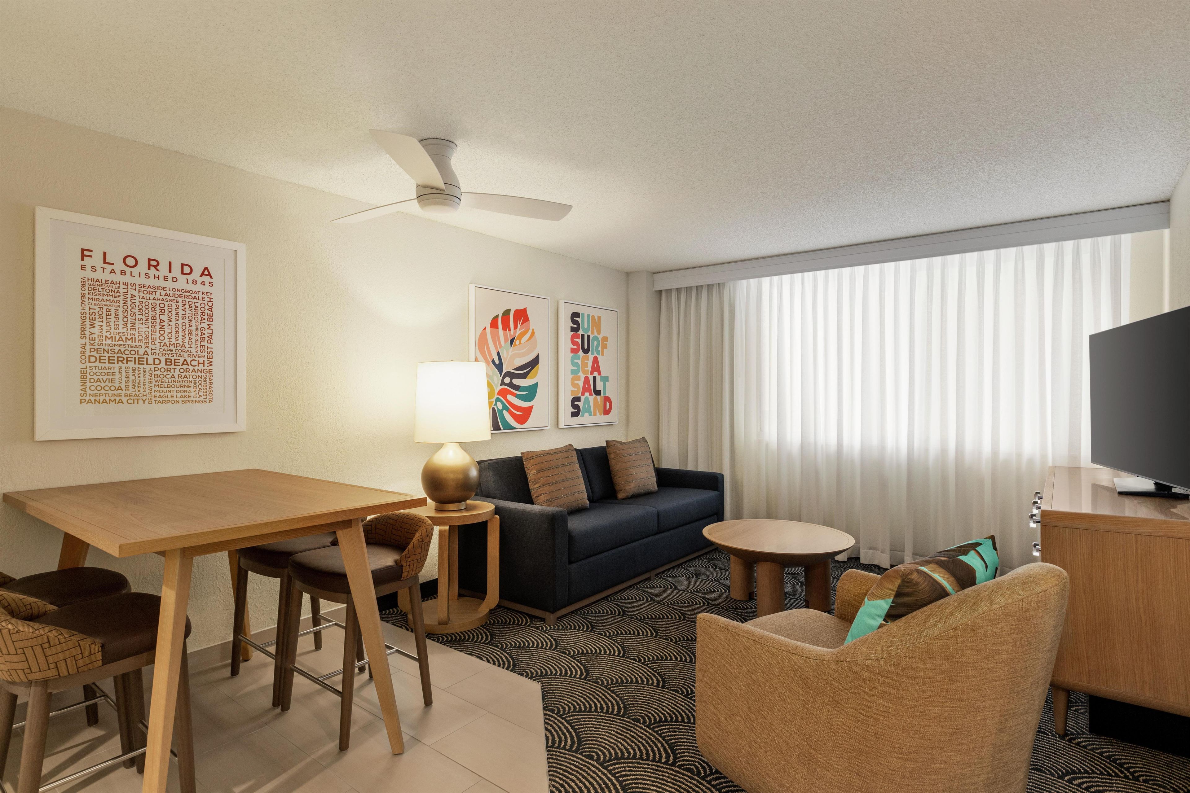 A hotel room with a dining table, sofa, armchair, and a TV.