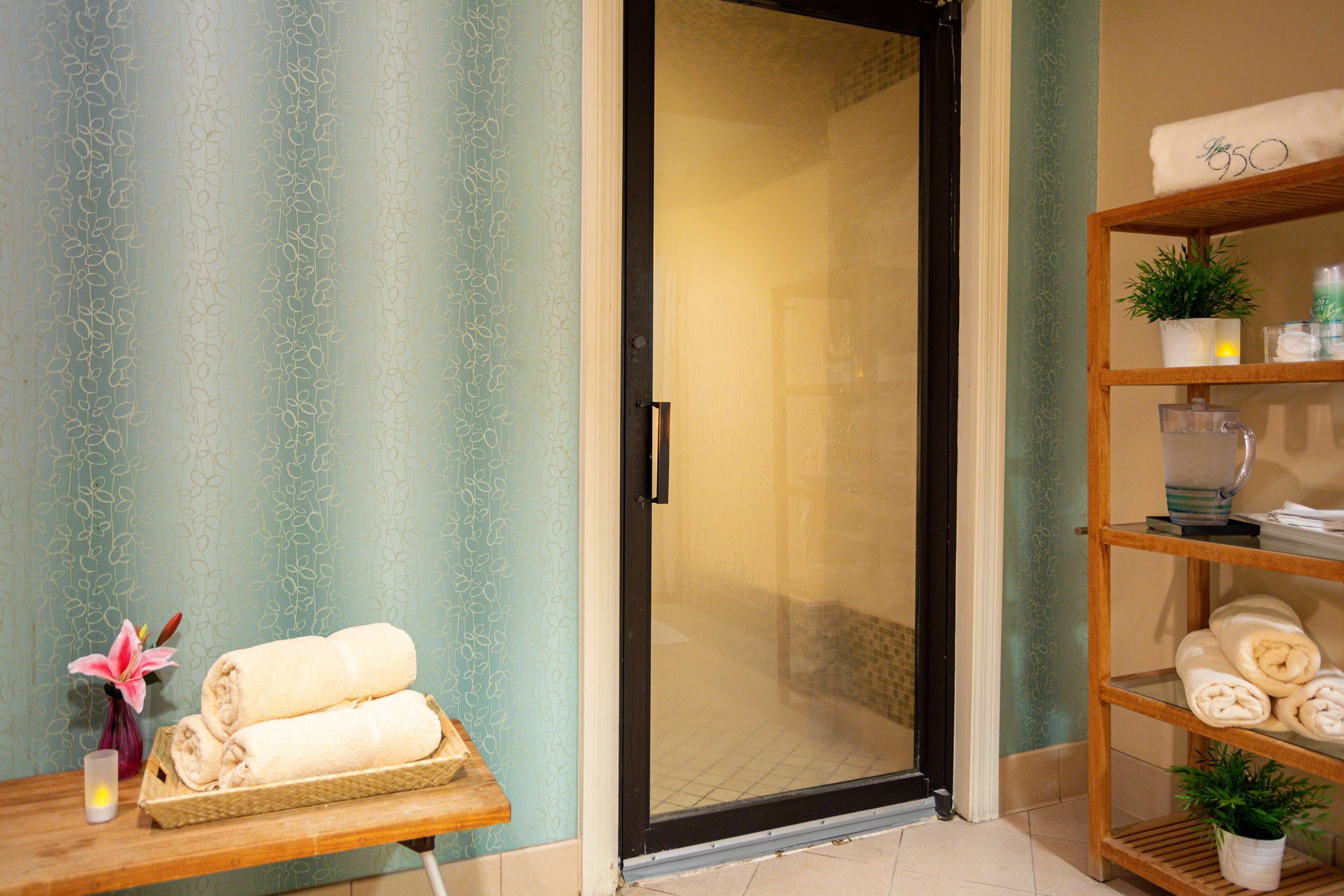 A bathroom with a glass shower door, a wooden shelf with towels, and a vase with a flower.