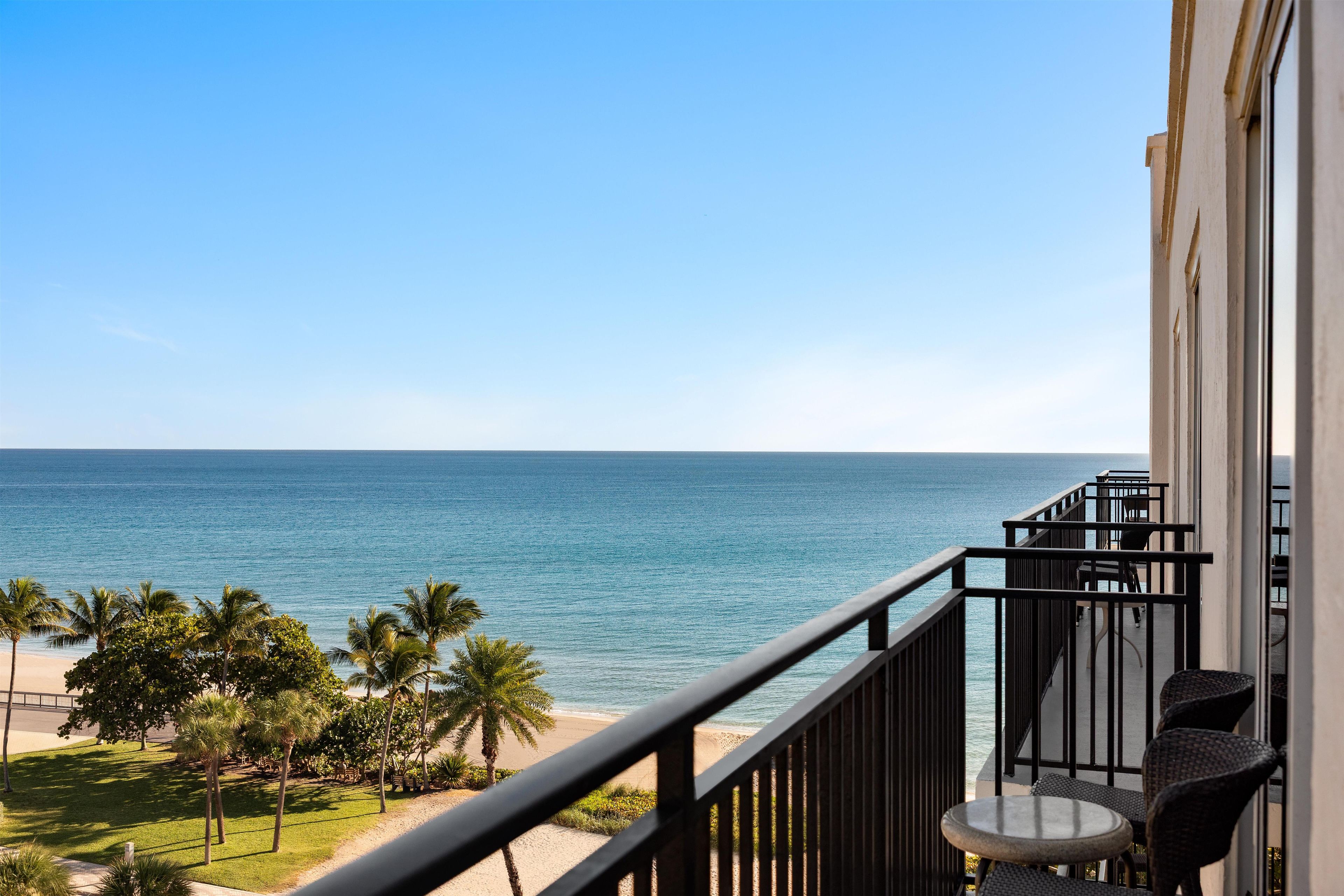 A balcony with a view of the ocean and palm trees.