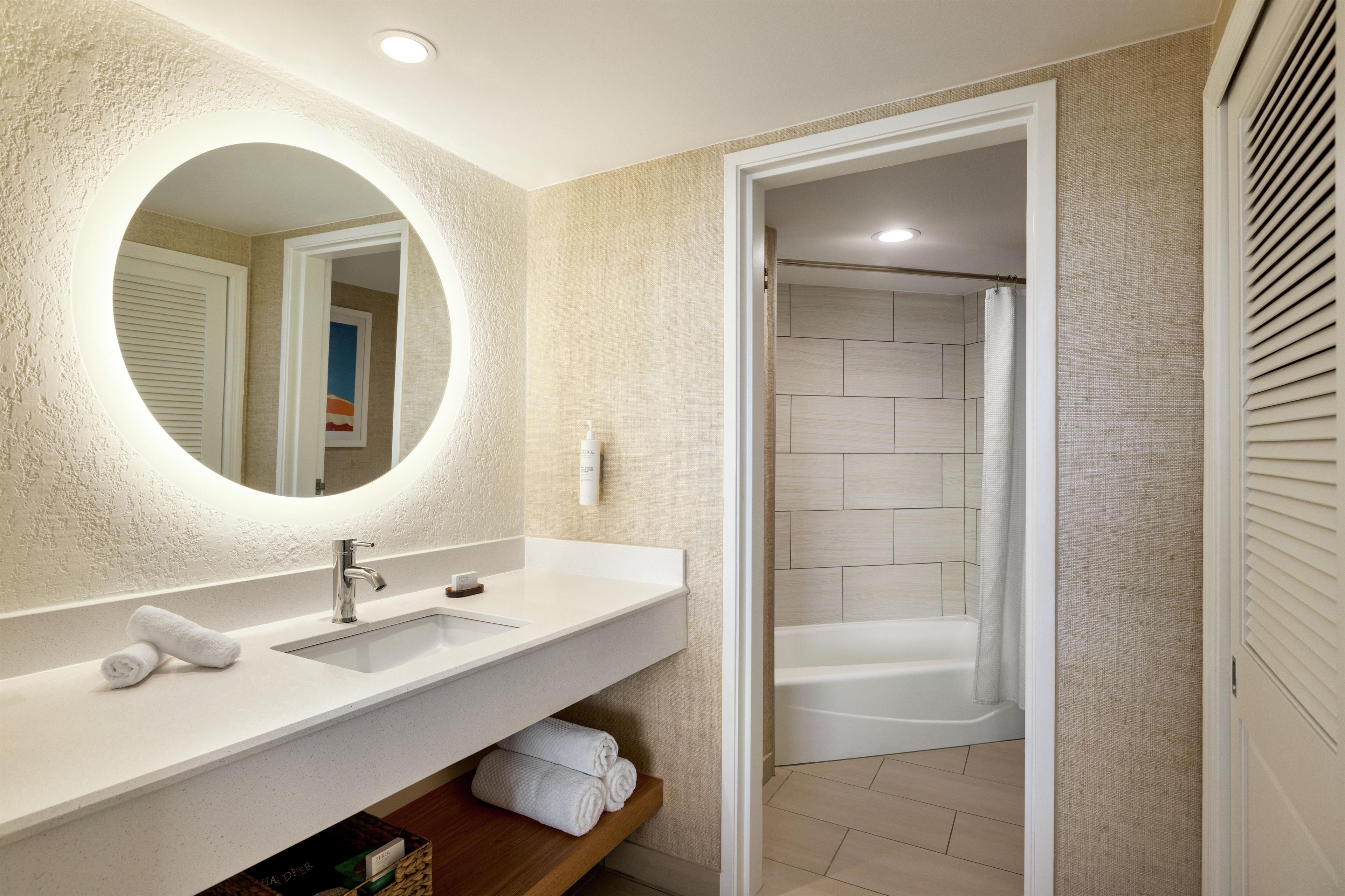 Un baño con lavamanos blanco, espejo y zona de ducha.