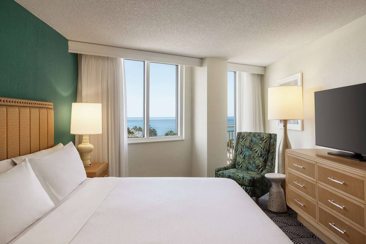 Ein Hotelzimmer mit einem großen Bett, einem Fernseher, einem Sessel und Meerblick.