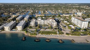 Vista aérea de un complejo hotelero costero con varias construcciones, una playa y aguas azules cristalinas.