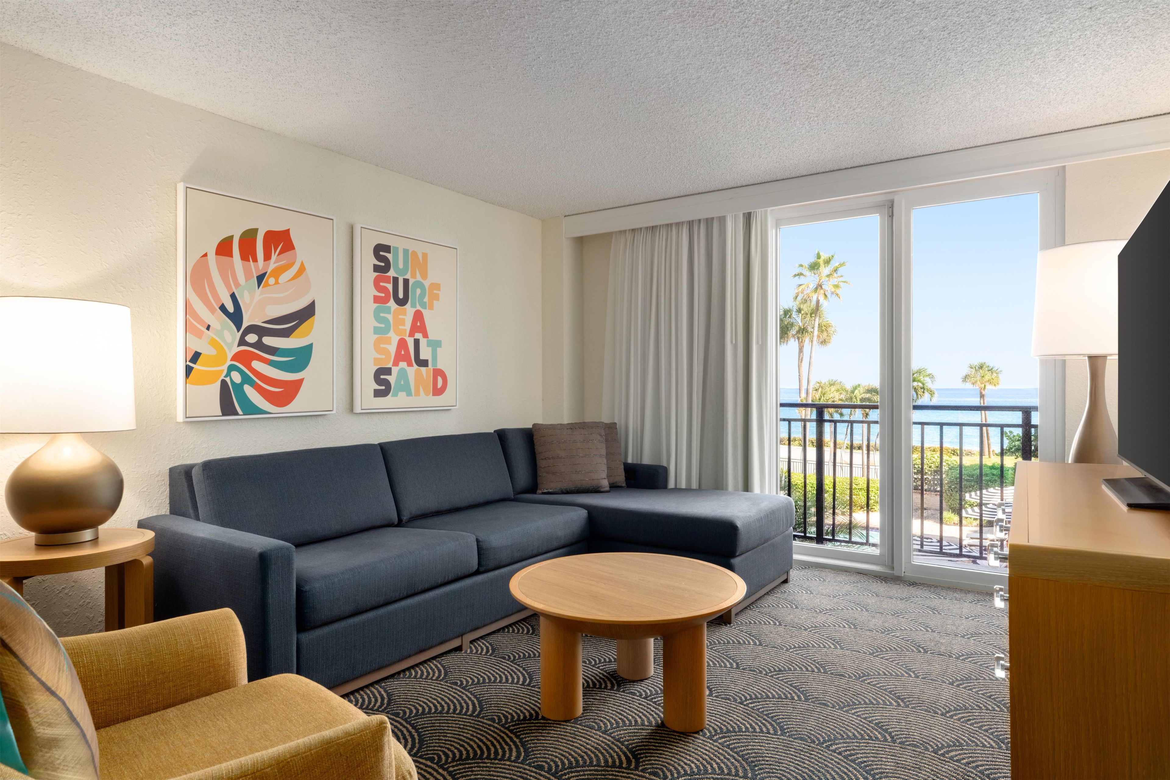 A hotel room with a sofa, a round table, a TV, and artwork on the wall.