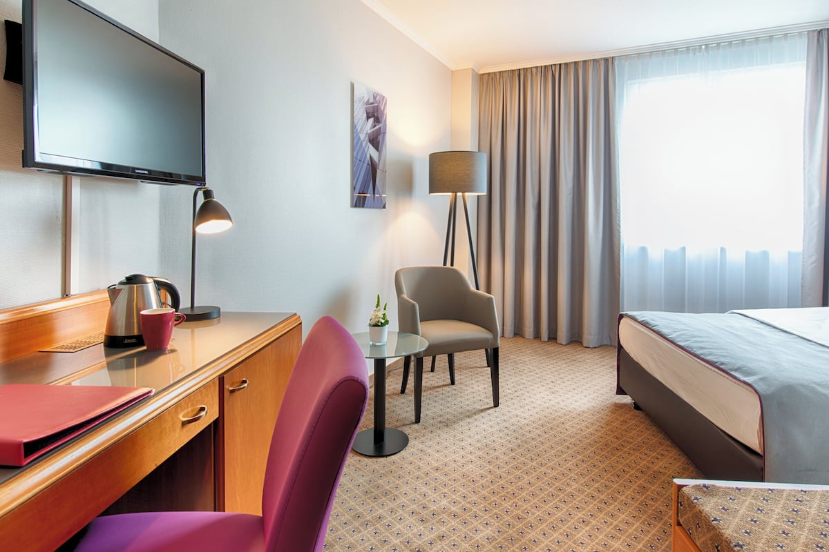 Une chambre d’hôtel équipée d’un lit, d’un bureau avec un ordinateur, d’une chaise, d’une lampe et d’un téléviseur.