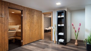 Une salle de spa moderne dotée d’un sauna en bois, d’un espace dédié aux massages et d’une étagère noire où sont rangées les serviettes.