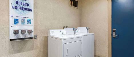 A laundry area with two white washers and dryers, a blue door, and a sign advertising soap, bleach, and softeners.