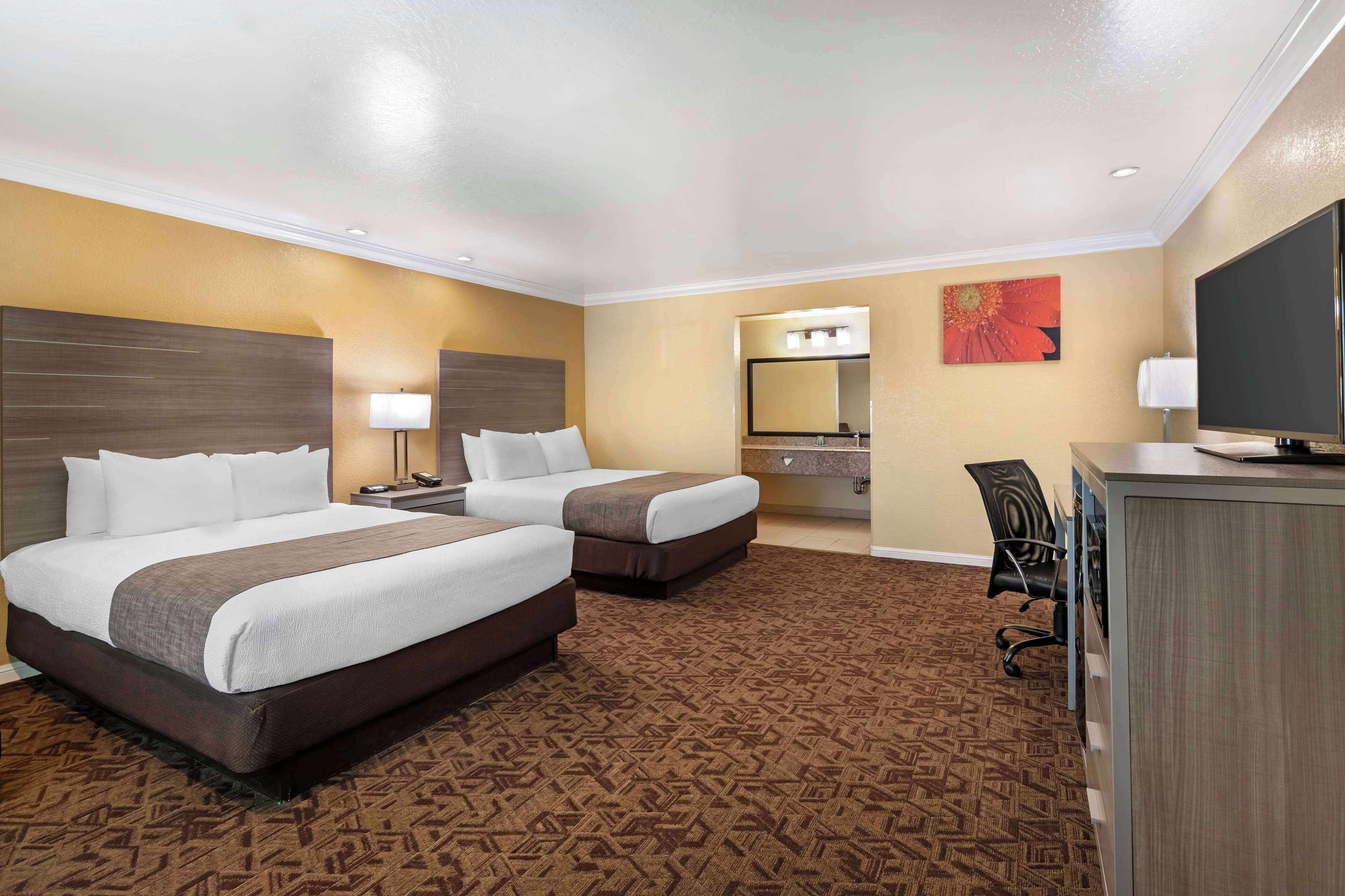 A hotel room with two beds, a desk, a TV, and a bathroom visible through an open door.