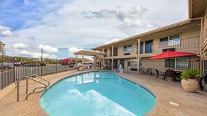 A swimming pool with a 6 feet depth marker, surrounded by a covered patio area with outdoor seating and a red umbrella. - Best Western Hanford Inn (Hanford)