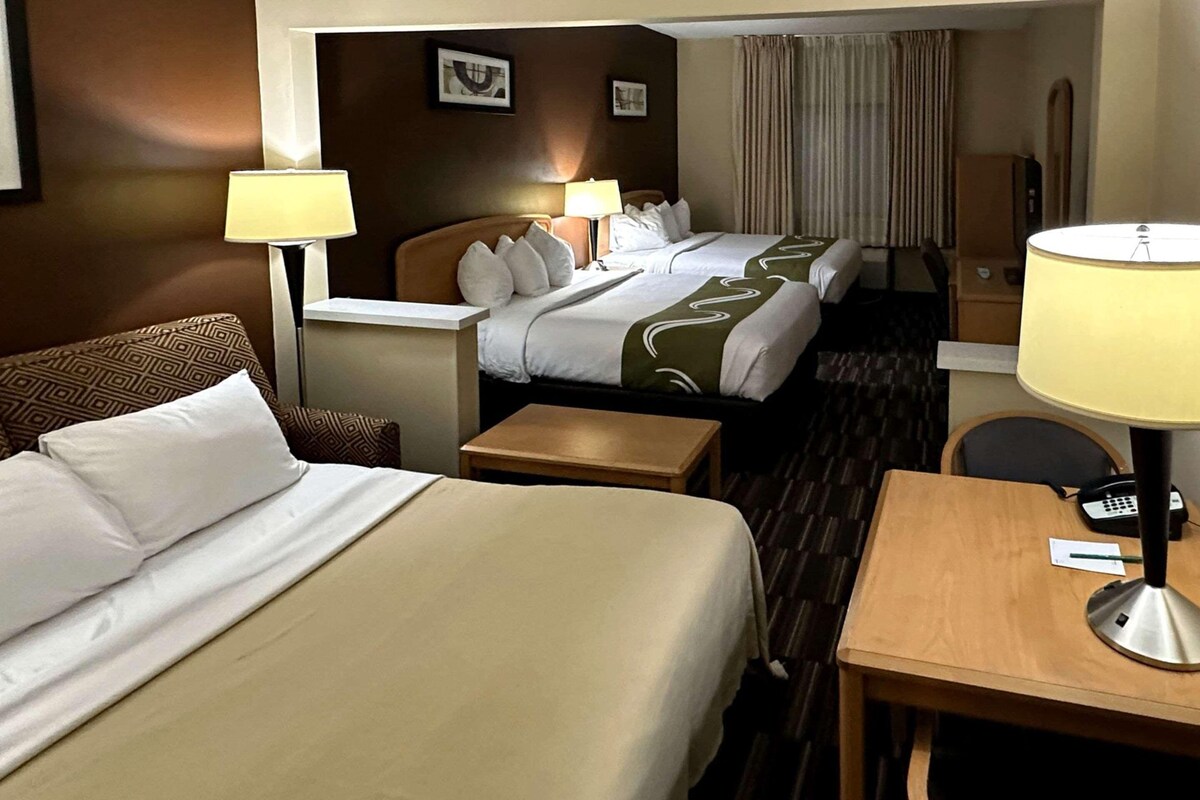 Una habitación de hotel con dos camas, un escritorio, una silla, una lámpara y un teléfono.