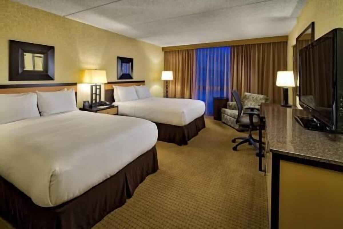 A hotel room with two beds, a desk, a chair, and a television.