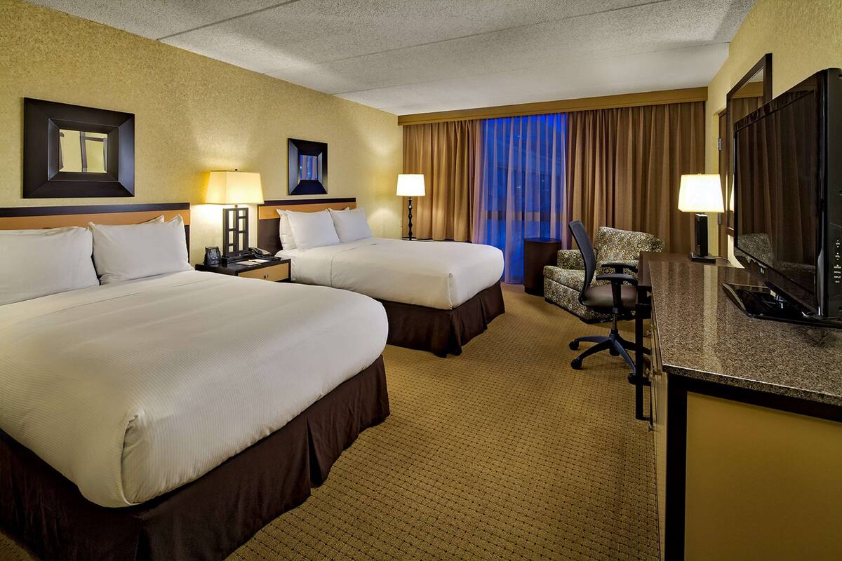 A hotel room with two beds, a desk with a TV, and a chair.