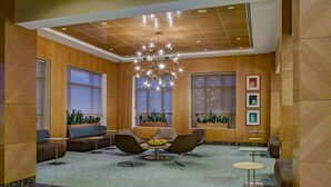 A modern lobby with wooden paneling, a chandelier, seating area, and potted plants. - DoubleTree by Hilton Chicago - Arlington Heights (Arlington Heights)