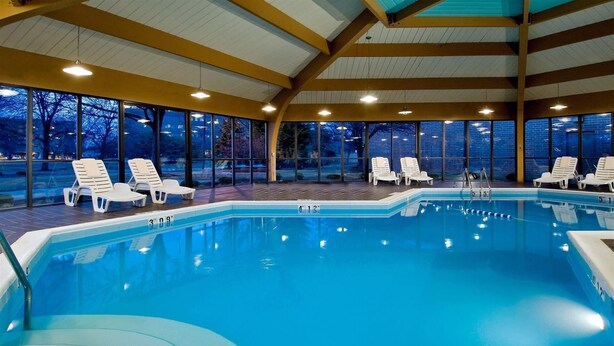 An indoor swimming pool with clear blue water, surrounded by white lounge chairs and large windows offering views of the outside. - DoubleTree by Hilton Chicago - Arlington Heights (Arlington Heights)