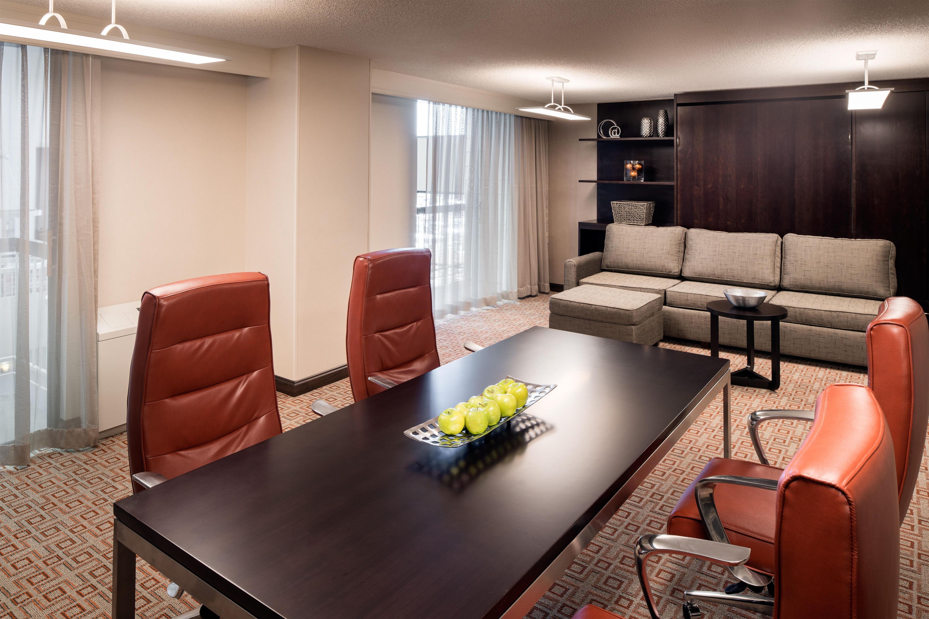 A hotel room with a dining table, two chairs, a sofa, and a small coffee table.