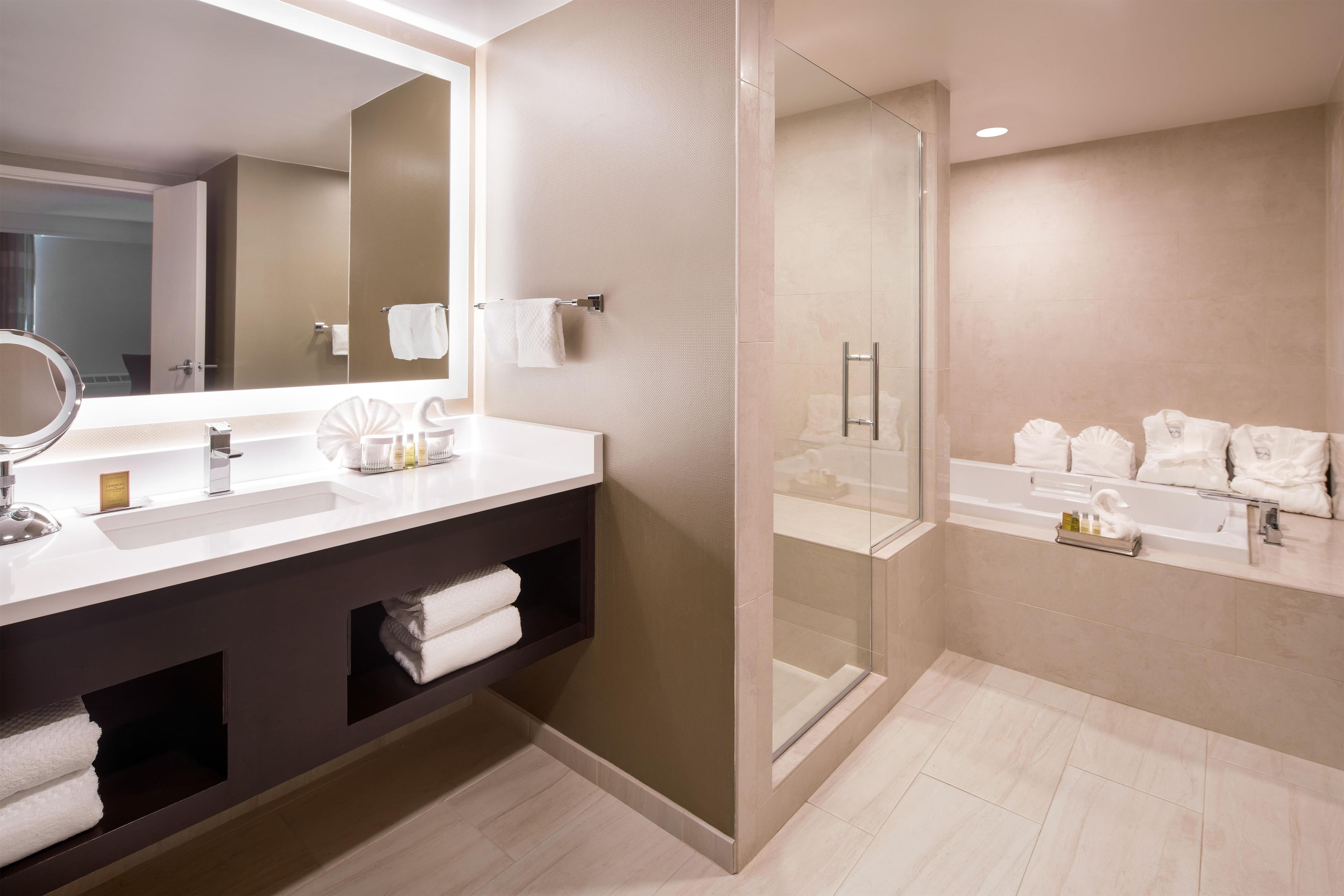 A modern bathroom with a large mirror, a vanity with a sink, a shower area, and a bathtub.