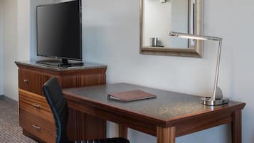 A hotel room with a wooden desk, a television, a mirror, and a lamp.