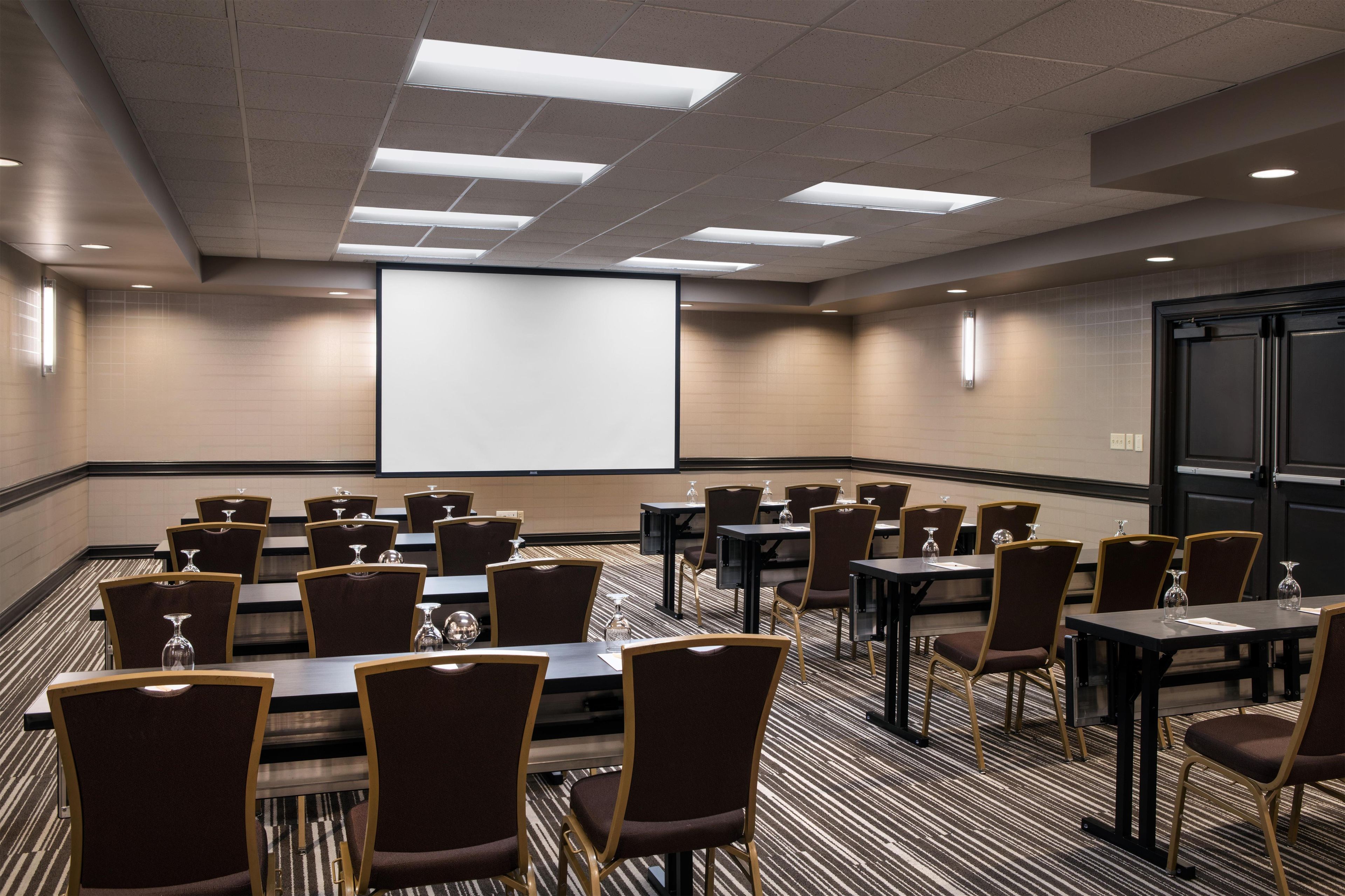 A conference room with a large projection screen, multiple tables, and chairs.