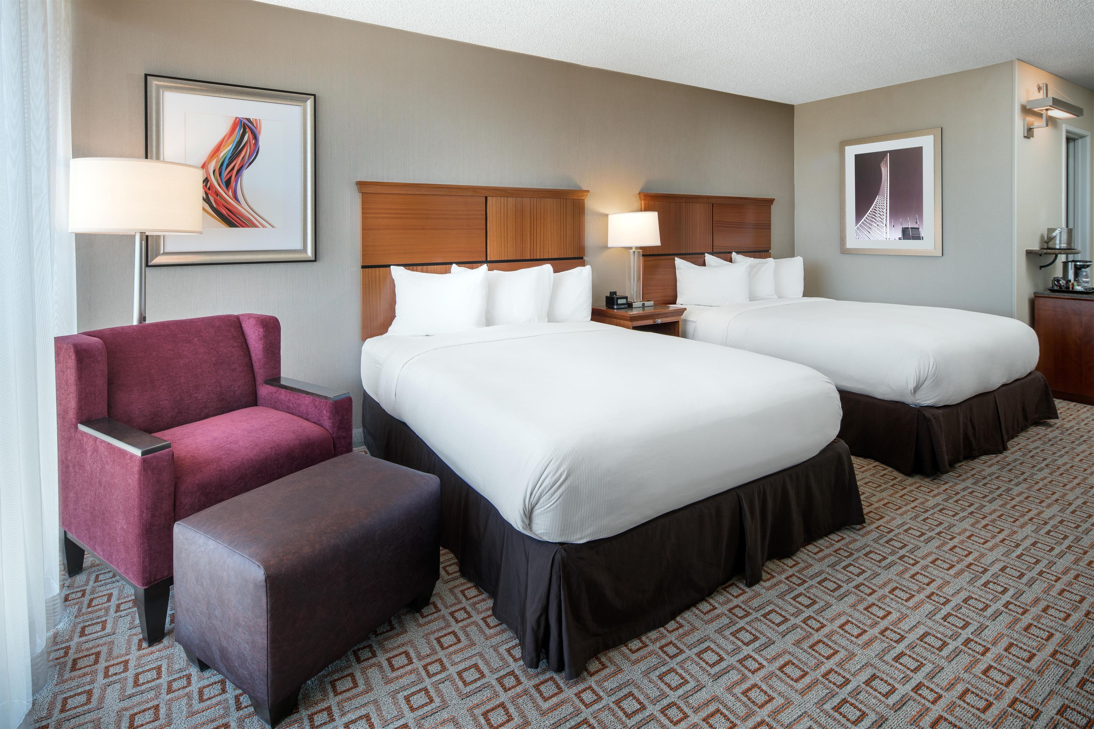 A hotel room with two beds, a desk, a chair, and artwork on the walls.