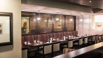 A restaurant with a long dining table, multiple chairs, and a patterned bench.