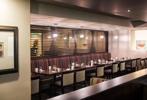 A restaurant with a long dining table, multiple chairs, and a patterned bench. - DoubleTree by Hilton Denver Tech Center (Greenwood Village)