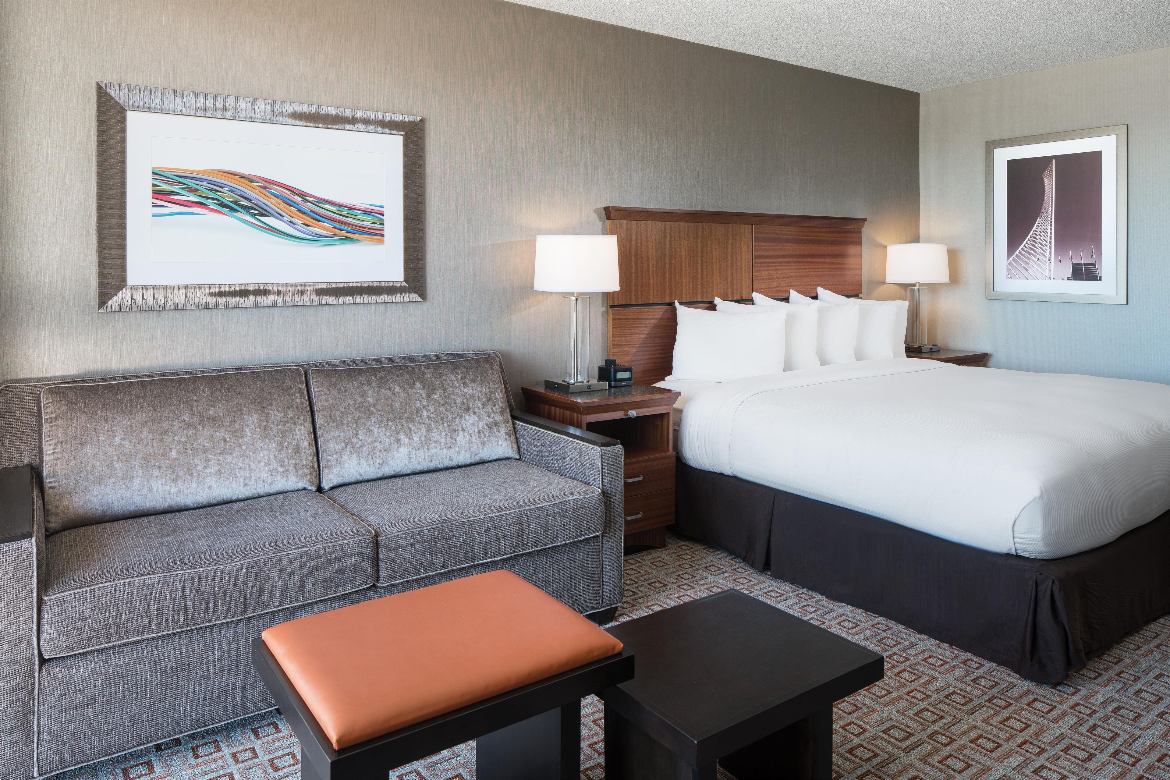 A hotel room with a bed, a sofa, a nightstand, a lamp, and a framed picture on the wall.