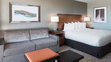 A hotel room with a bed, a sofa, a nightstand, a lamp, and a framed picture on the wall.