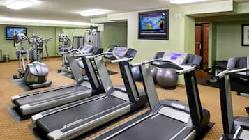A gym with Nautilus treadmills, elliptical machines, and a TV screen displaying a workout video.