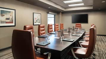 A conference room with a long table, leather chairs, a flat-screen TV, and artwork on the walls.