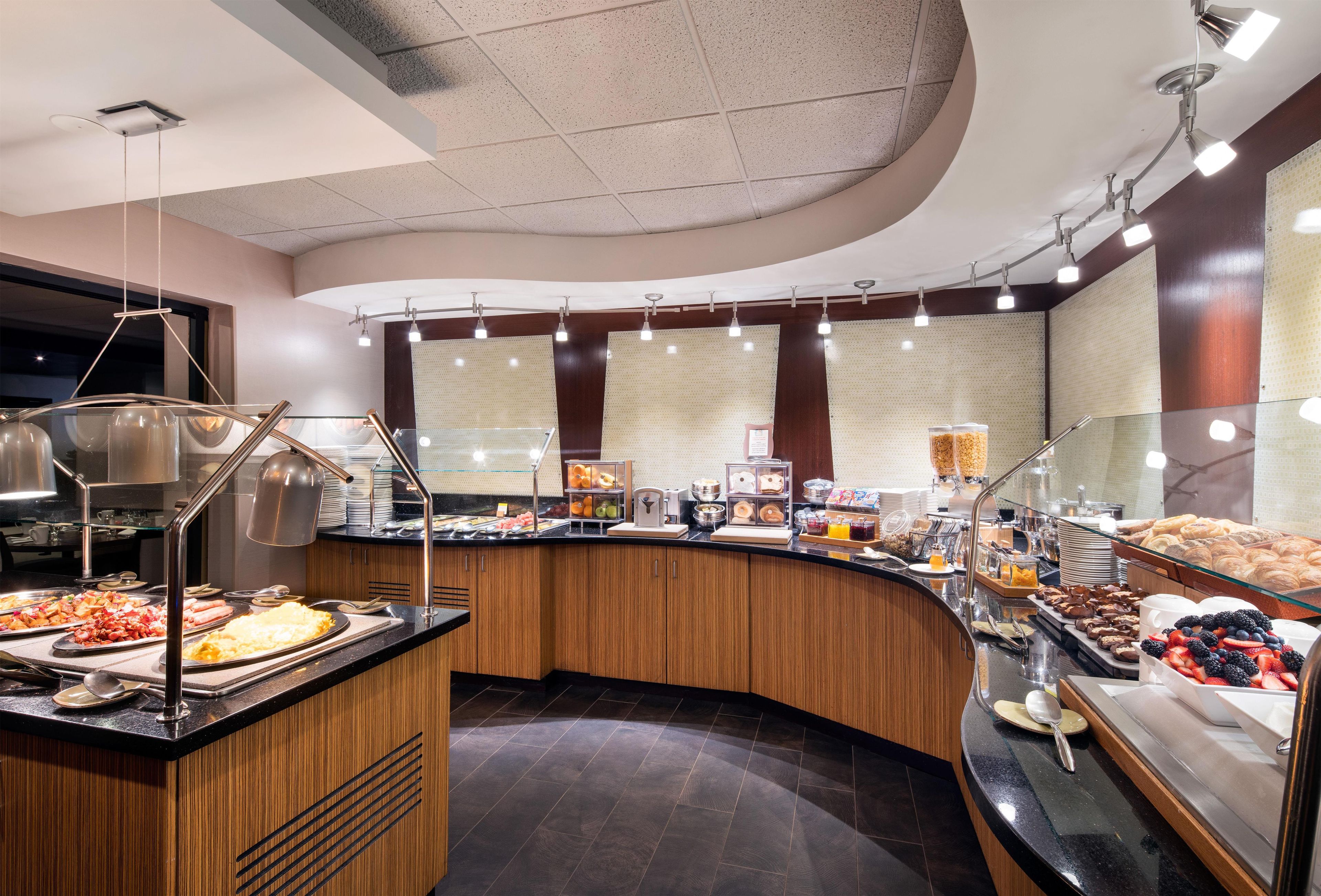 Un espace buffet proposant une variété de plats, un coin café et un espace détente avec un mur incurvé et des luminaires au plafond.