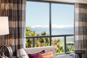 A room with a large window offering a mountain view, a sofa with cushions, and a small table. - DoubleTree by Hilton Denver Tech Center (Greenwood Village)