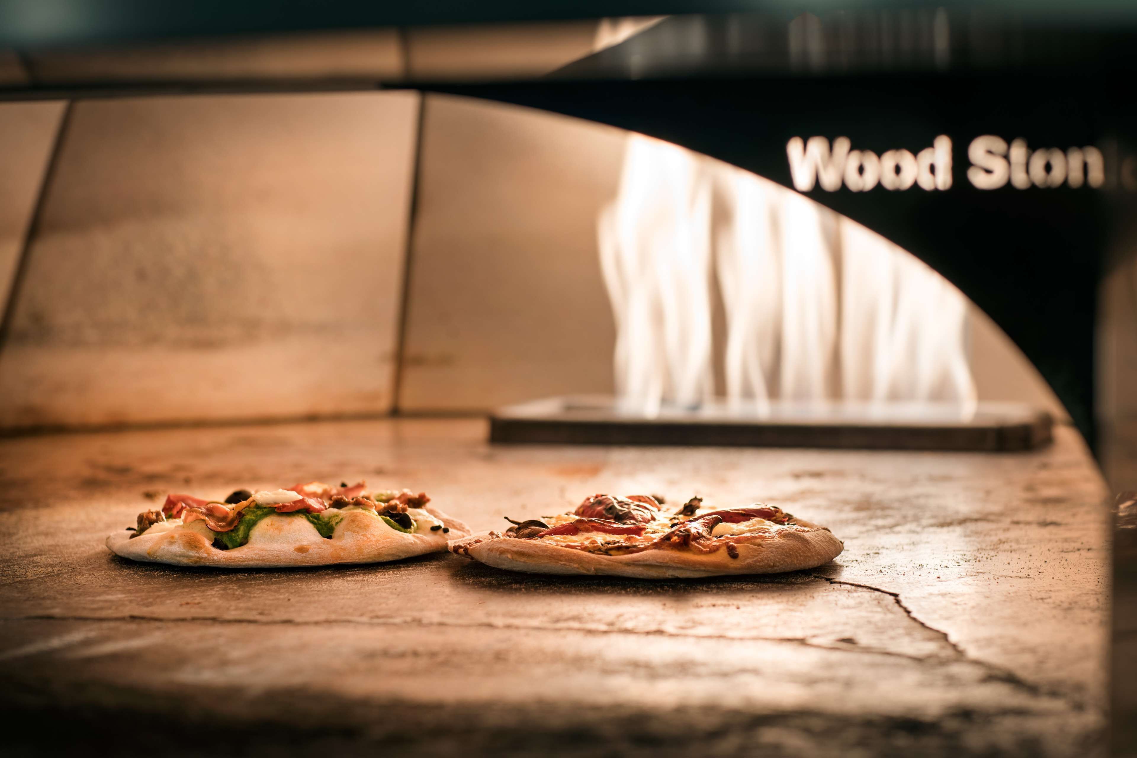 Two pizzas on a wooden surface with a wood stonemason's tool in the background.