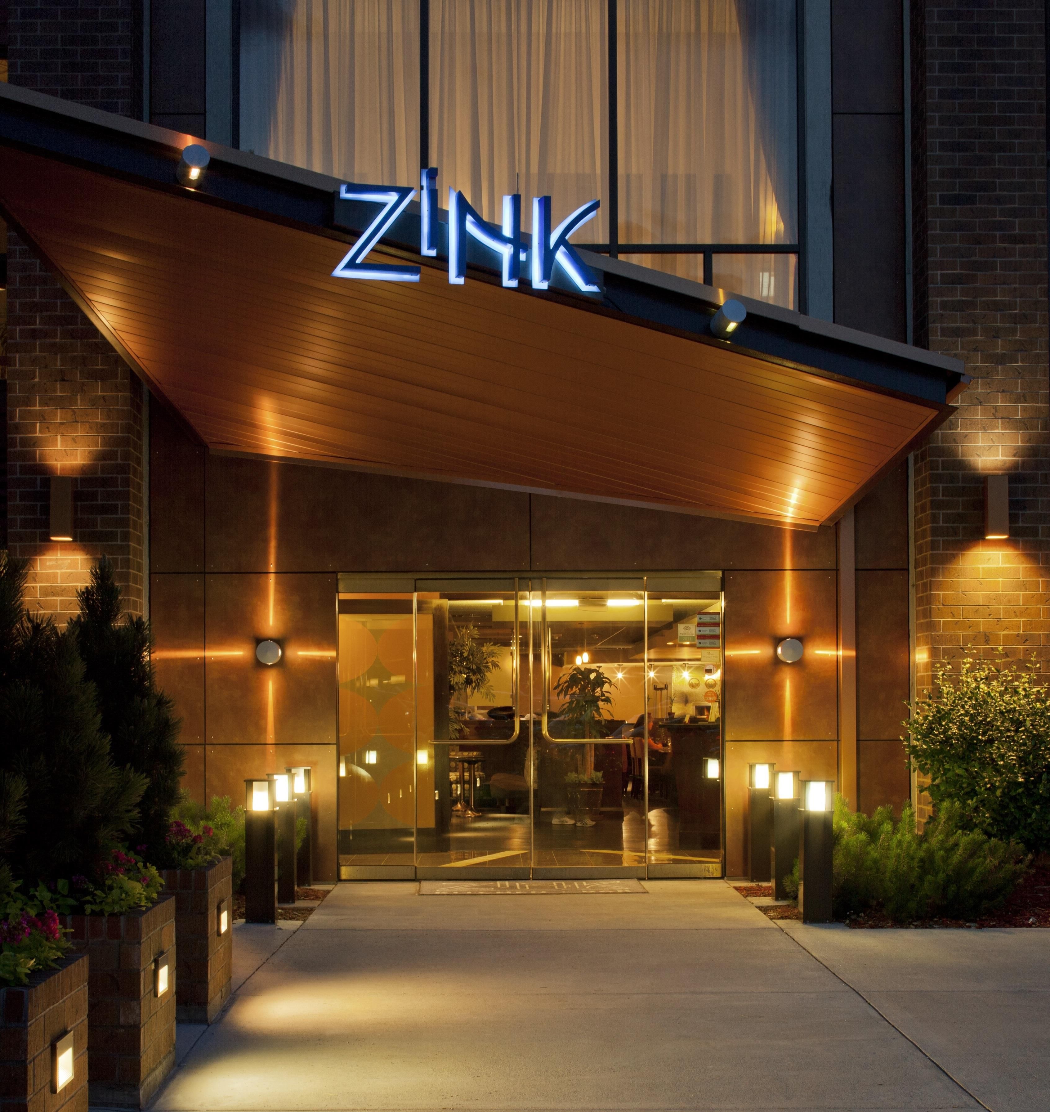 A hotel entrance with a modern design, featuring a prominent illuminated sign and a glass door entrance.