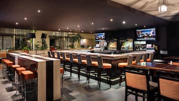 A bar area with multiple seating options, including bar stools and tables, and a television screen mounted on the wall.