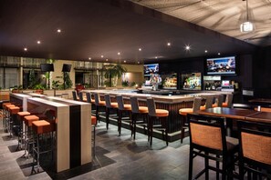 A bar area with multiple seating options, including bar stools and tables, and a television screen mounted on the wall. - DoubleTree by Hilton Denver Tech Center (Greenwood Village)