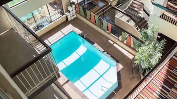 A swimming pool with a tiled deck, surrounded by a multi-level balcony with railings and potted plants.