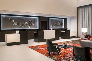 A modern hotel lobby with two reception desks, a seating area with chairs, a patterned rug, and a large window with curtains. - DoubleTree by Hilton Denver Tech Center (Greenwood Village)